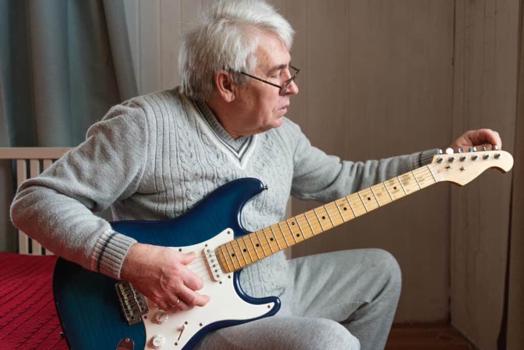Senior man sitting on sofa learning to play guitar